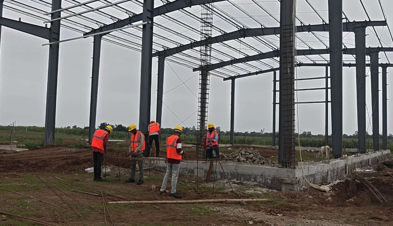 Workers beside a steel structural frame at the Guna compressed biogas plant construction site